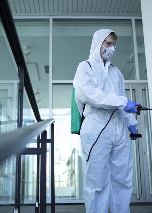 Unrecognizable person in white protection suit disinfecting public areas to stop spreading highly contagious corona virus.
